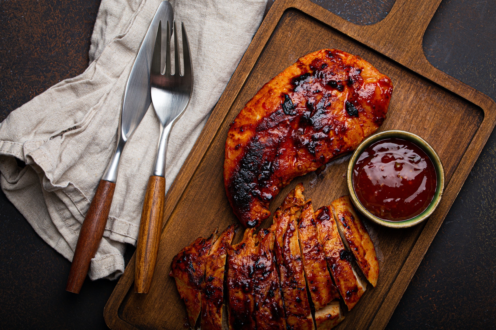 Grilled turkey or chicken fillet with red sauce served and sliced on wooden cutting board