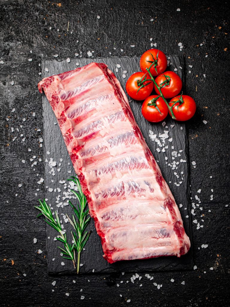 Raw ribs on a stone board with tomatoes and pieces of salt.