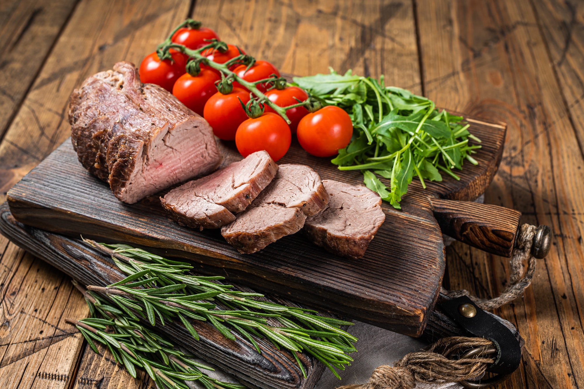 Roast Veal tenderloin, sliced Roastbeef on wooden board with garnish. Wooden background. Top view