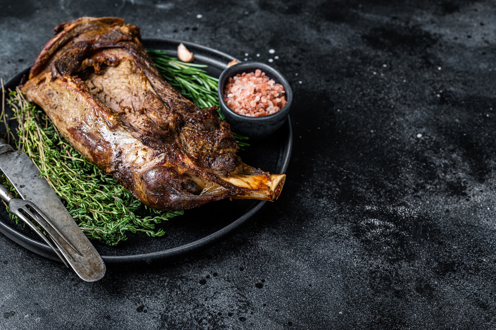 Roasted lamb mutton shoulder meat on a plate with knife and fork. Black background.